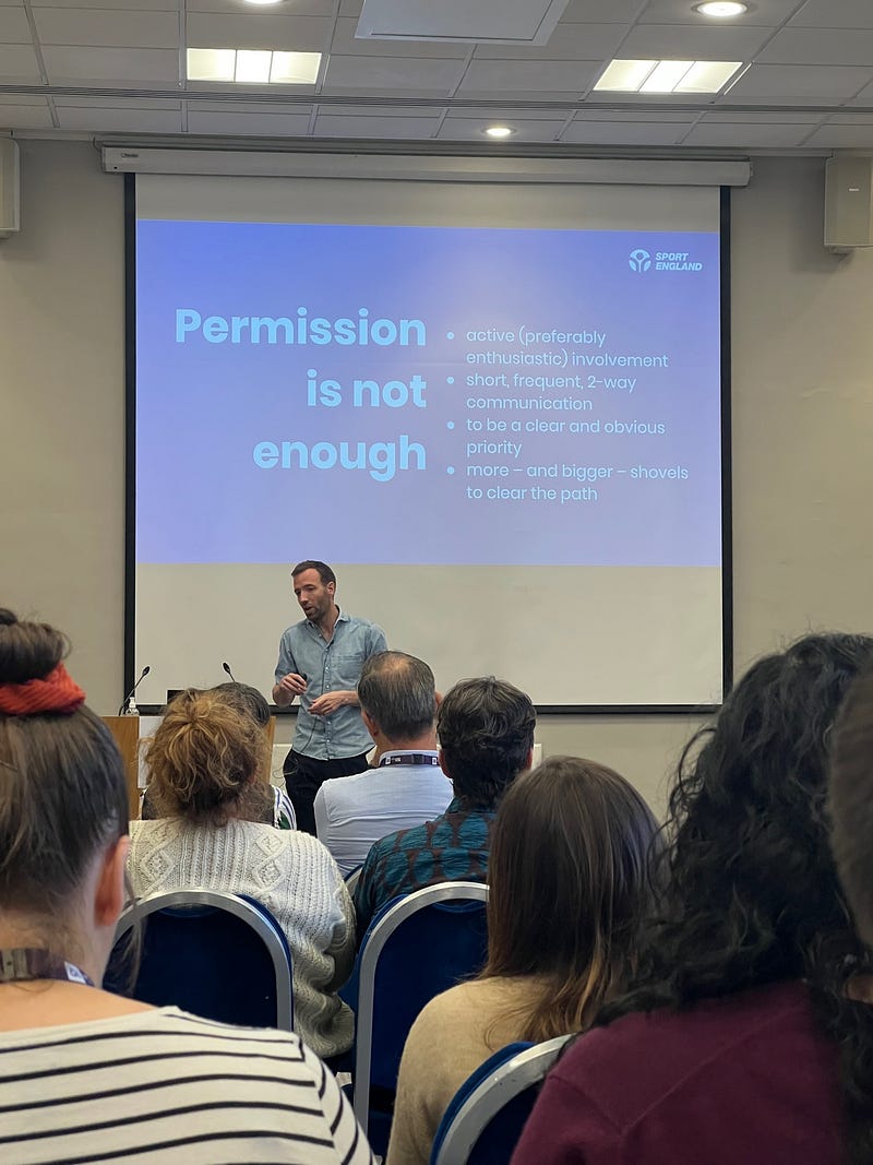 Steven Garrett stands in front of a slide that reads: “permission is not enough. [you need] active (preferably enthusiastic) involvement; short, frequent two way communication; to be a clear and obvious priority; and more — and bigger — shovels”