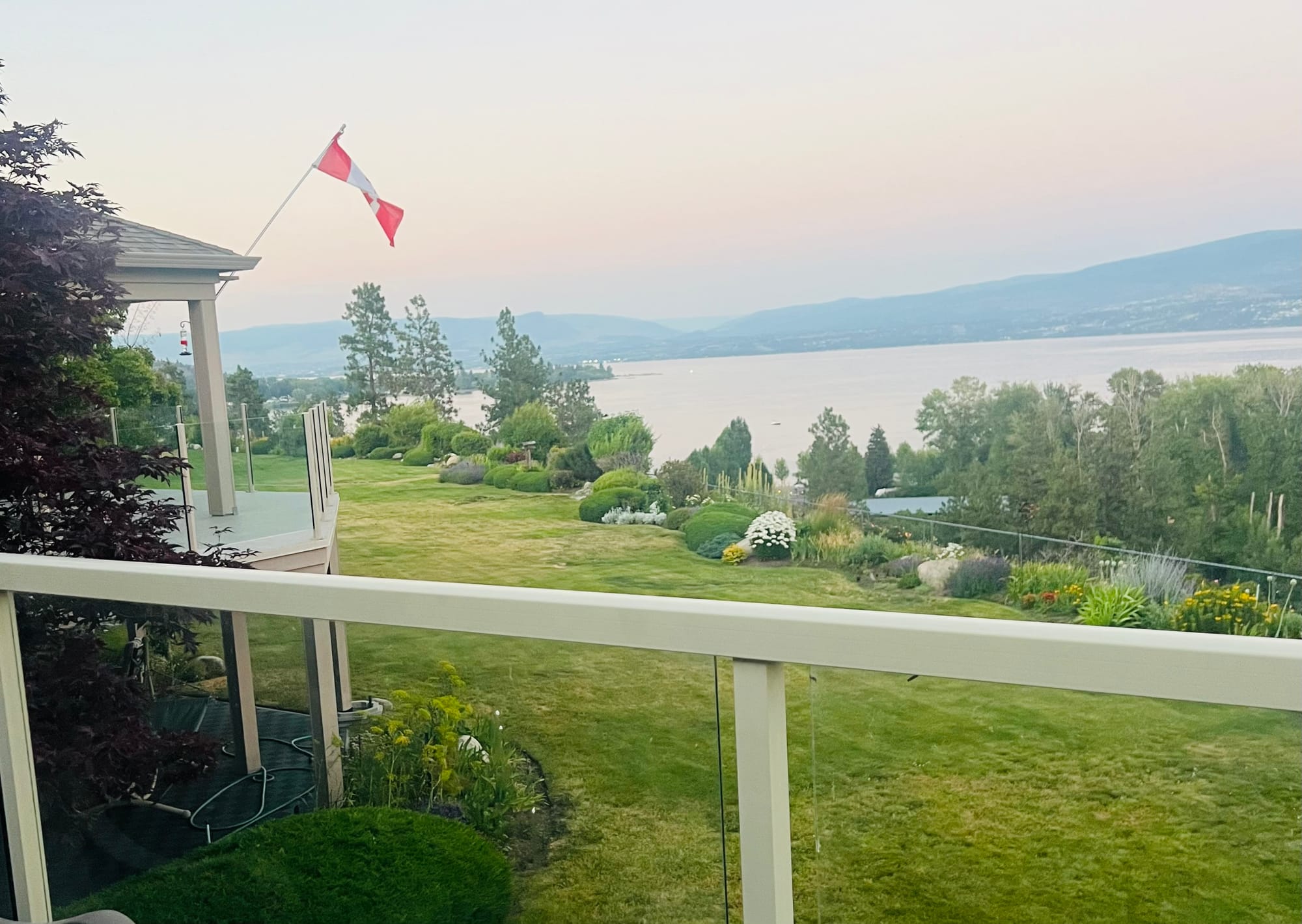 View of a green lawn and plants, with a large lake and mountains in the background