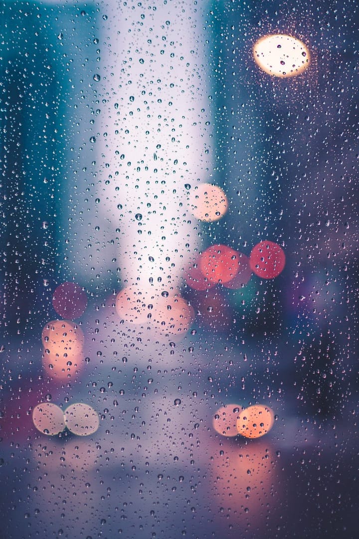 Rain on a window with pink and purple lights in the background