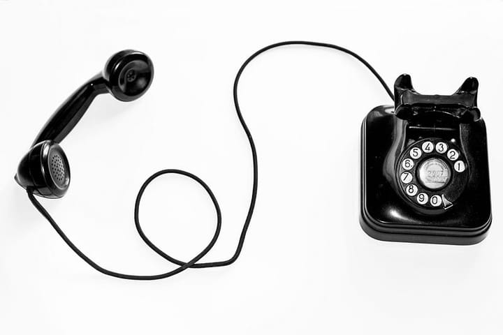 an older model black telephone on a white background. The receiver is next to the telephone