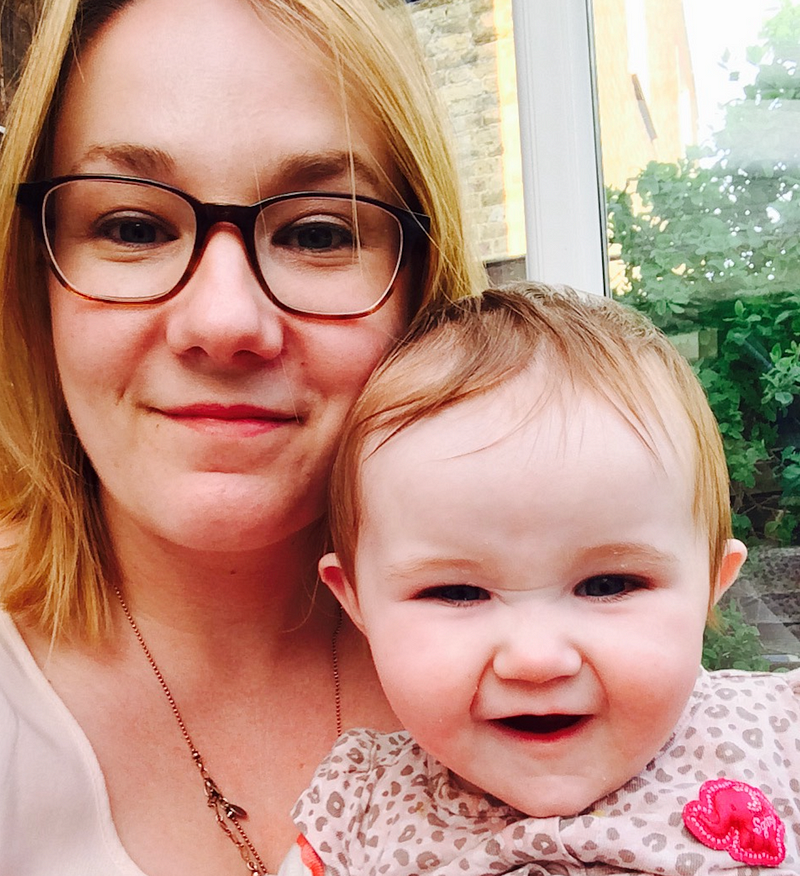 woman in glasses holds a baby who is launghing