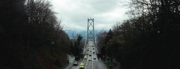 Image of the Lion’s Gate Bridge in Vancouver, with cars driving and trees and clouds surrounding