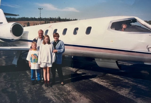 a family of four poses in front of a Lear Jet airplane. Father and mother in the back row and a teenage and child in the fron